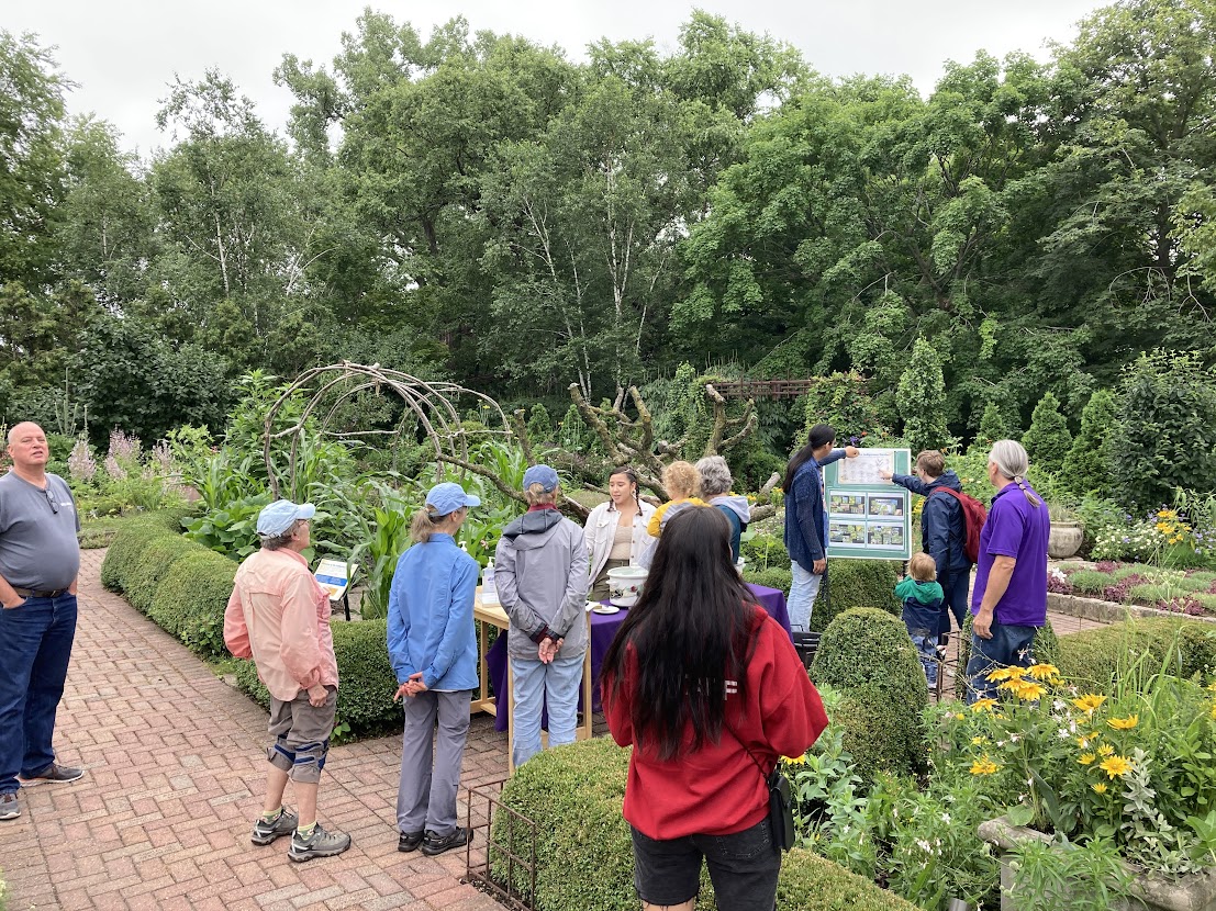 Un grupo de personas en un jardín escuchando una presentación.