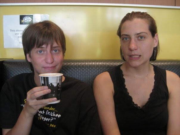 Dos adultos blancos se sientan en un asiento de restaurante.  El joven de la izquierda sostiene una taza y mira irónicamente a la cámara.  La joven, que es un poco más alta, mira a la cámara mostrando los dientes inferiores con una mirada de leve sorpresa.  Tienen caras de aspecto similar.